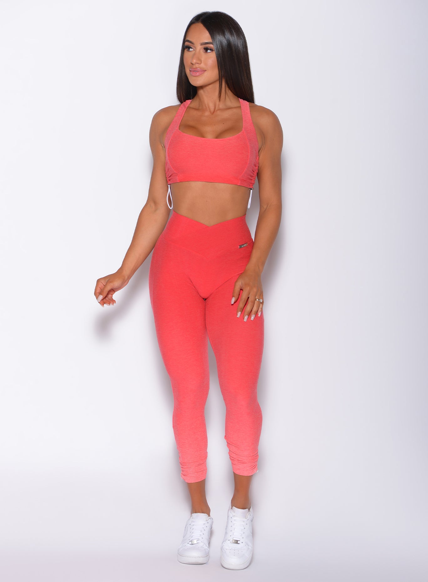 Front profile view of a model wearing our toggle leggings in Ombre Fiji Coral and a matching sports bra