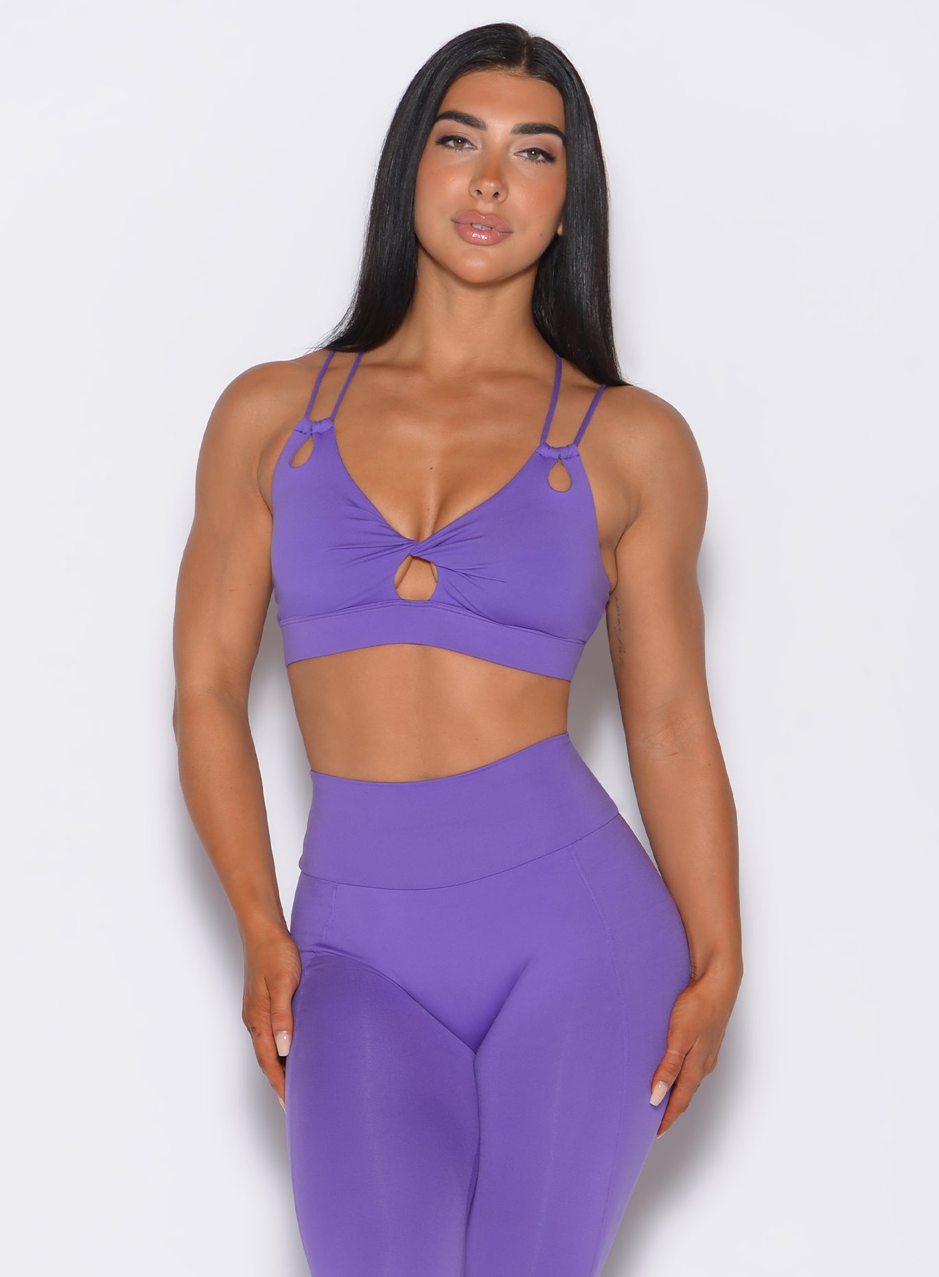 Front profile view of a model wearing our twist sports bra in royal purple color along with the matching shape leggings